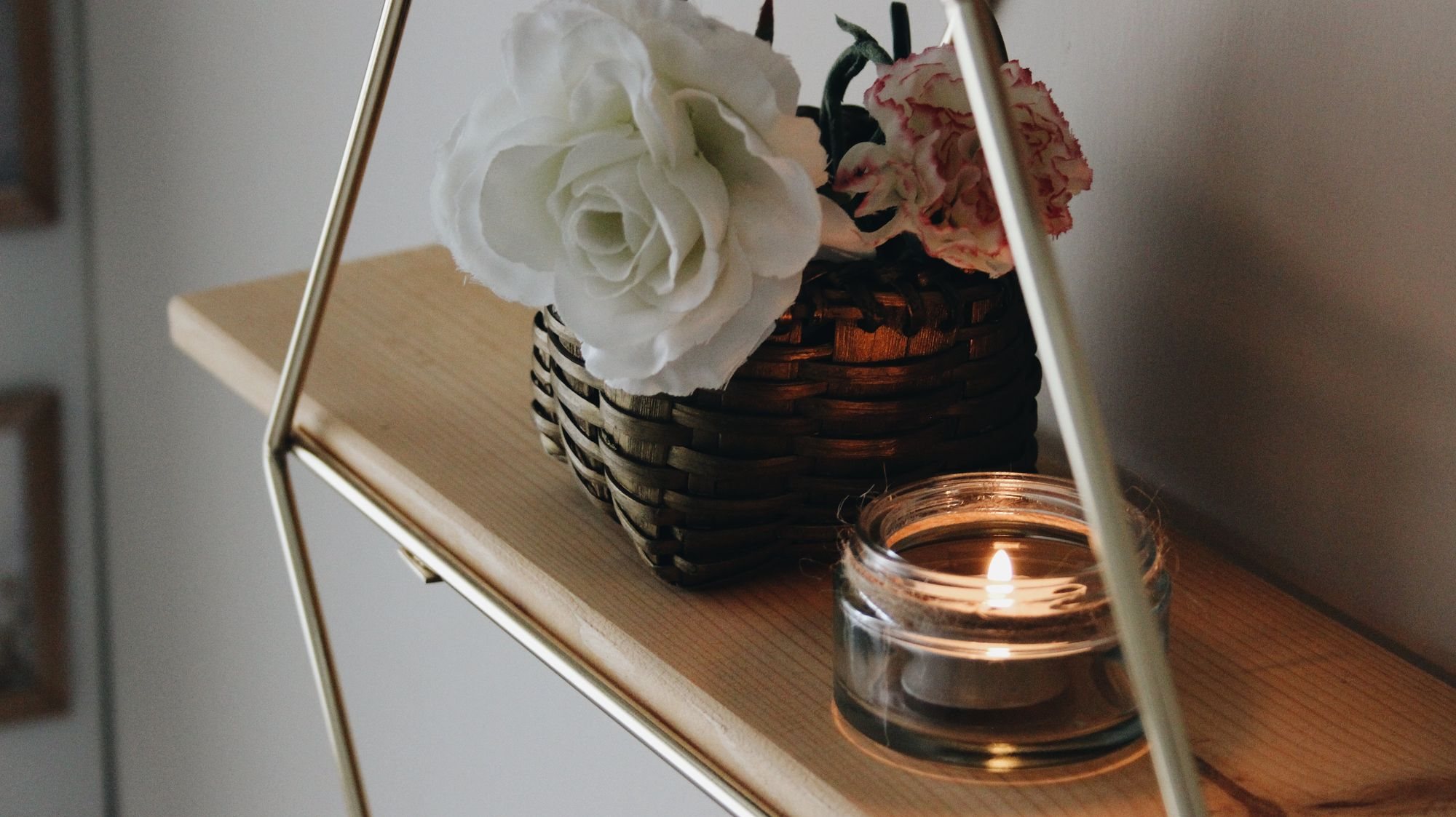 A lit candle beside a basket of white flowers